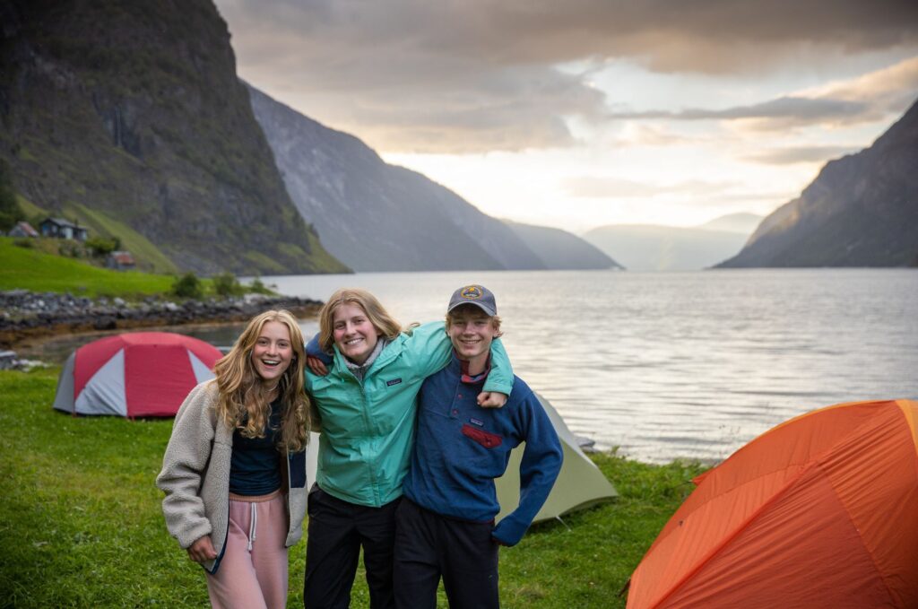 Smiling campers enjoy a lakeside campsite, reflecting the outdoor benefits of summer camps for kids.