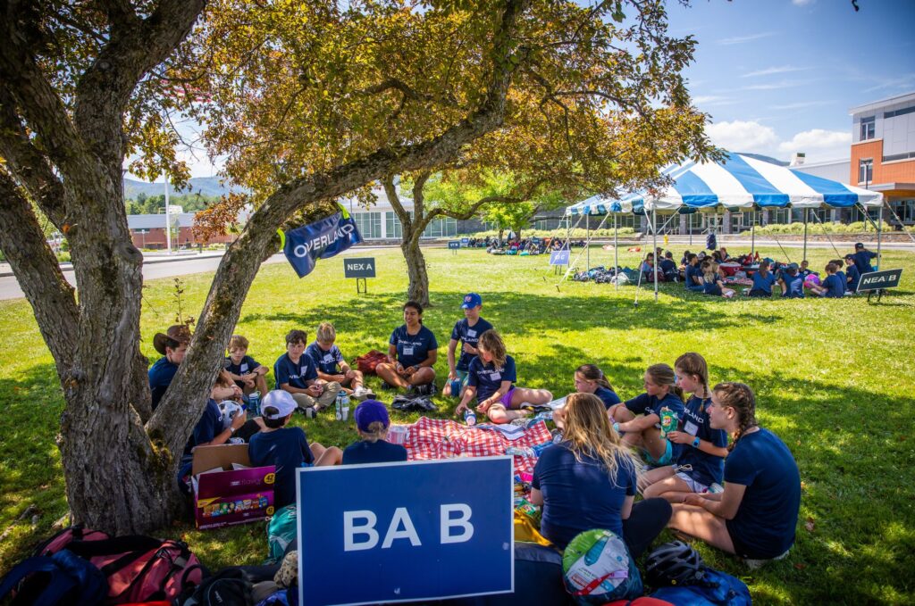 Campers gather for group activities under a tree, highlighting community-focused different types of summer camps.
