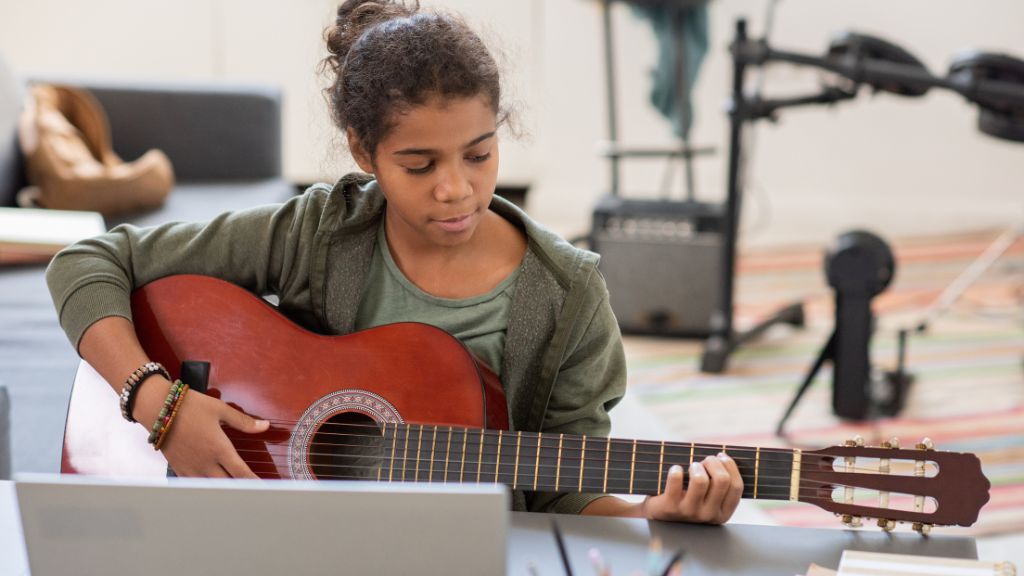 A young camper practices guitar in a cozy music room, focusing on chords and rhythm during a creative session at Music Camps.