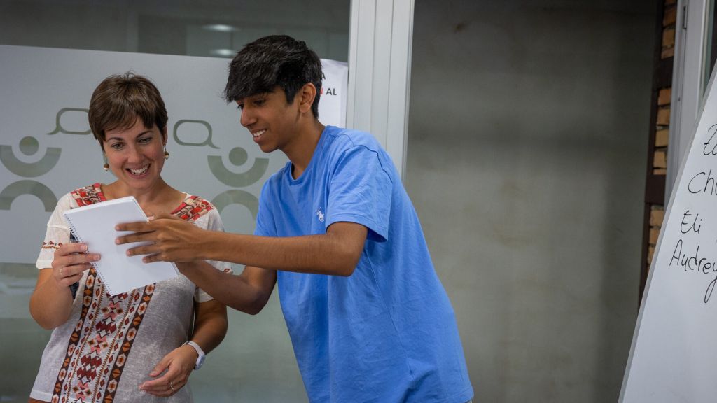 A student shares a notebook with a smiling teacher during an interactive lesson, highlighting connection and growth at Learning Language Camps.