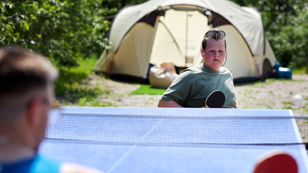 A camper focuses during a game of outdoor ping pong near a tent, enjoying inclusive activities and support at Special Needs Camps.