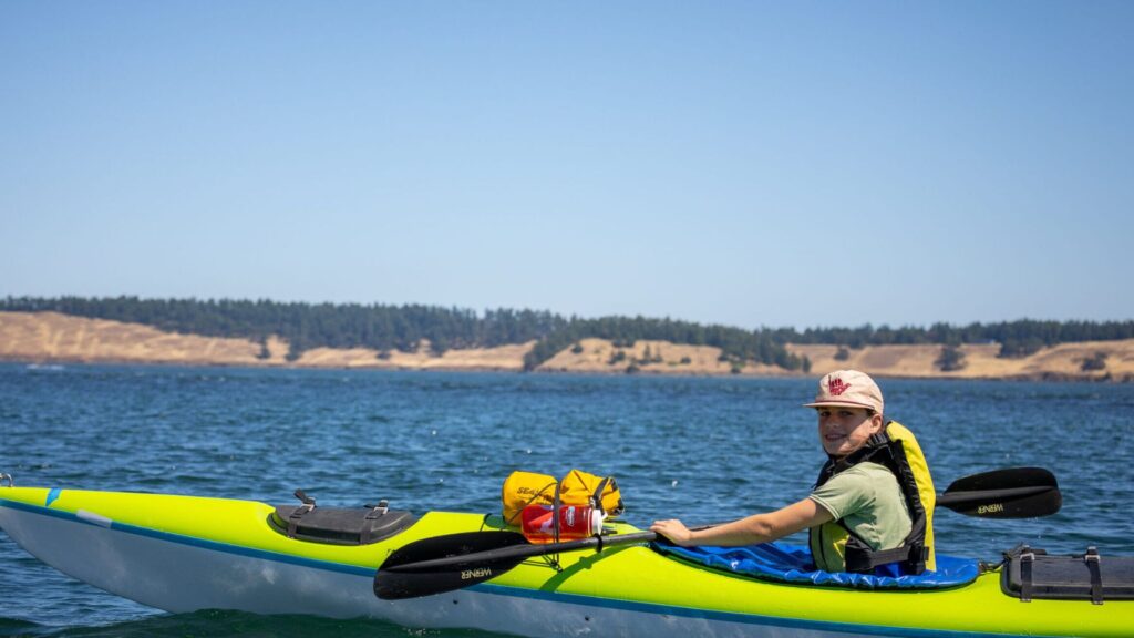 Child kayaking on a lake at summer camp, showing how to choose a summer camp based on activity type and outdoor adventure options.