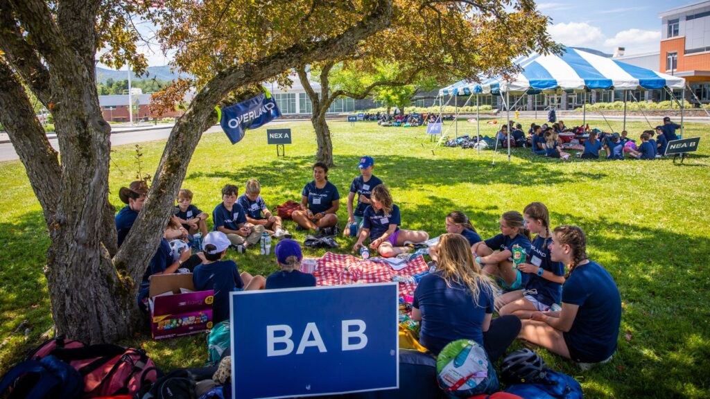 Campers sitting in groups under trees and tents during orientation, illustrating how camps organize enrollment and prepare kids for the experience ahead.