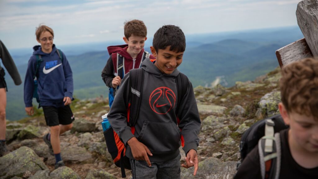 Campers leading a hike along a rocky mountain trail, gaining independence and confidence during summer camp preparation.