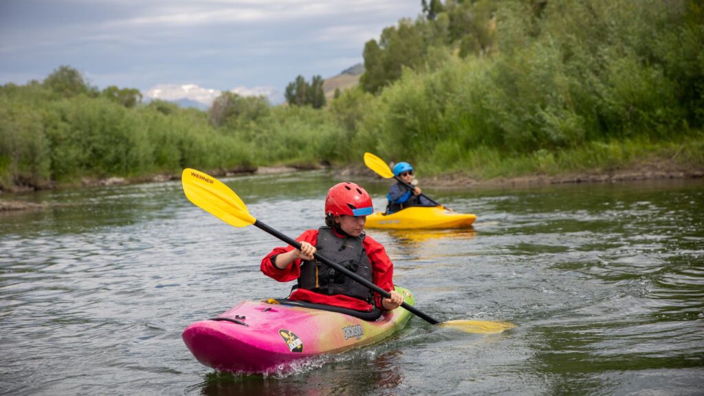 Kids kayaking on a river during summer camp, exploring outdoor adventure activities that match their interests.
