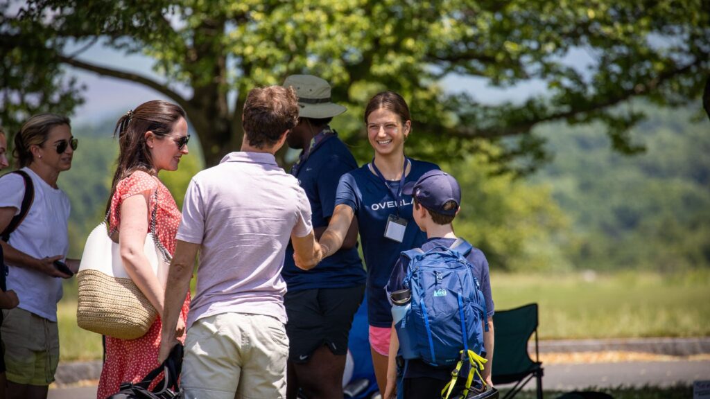 Camp staff greeting parents and campers outdoors while discussing medical or allergy information before summer camp begins.