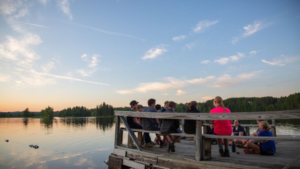 Teens from a Summer Travel Program sitting on a dock at sunset, sharing a group moment during an Overland Summers adventure.