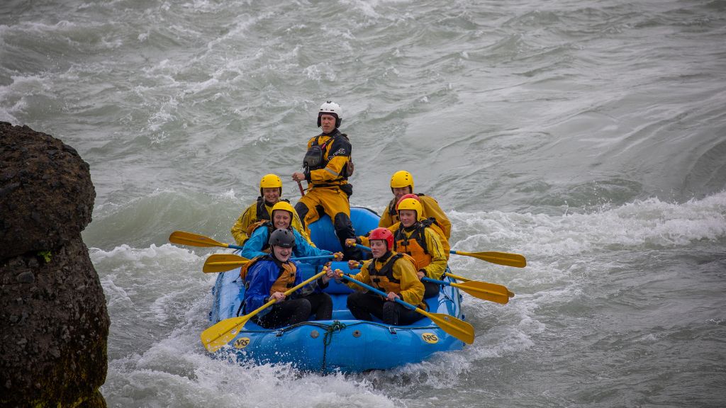 People in helmets and life jackets whitewater raft through rough river rapids, paddling together in an inflatable raft.