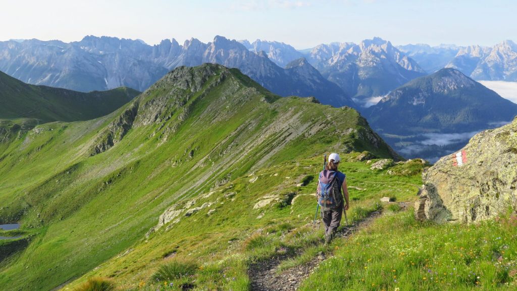 Hiker walks along a mountain trail with scenic peaks ahead, continuing forward despite the long and challenging path.