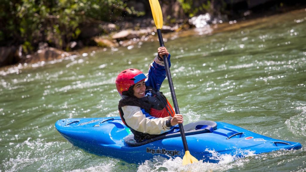 Summer camper kayaking through river rapids during an outdoor camp adventure