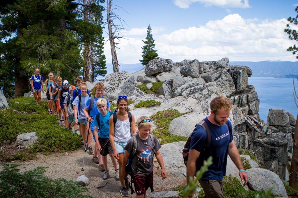 Overland Summers campers hiking together along a rocky lakeside trail.