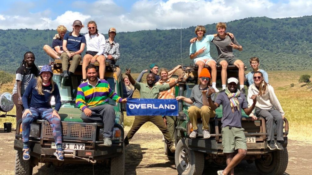 Teens and leaders posing by safari vehicles during the Kilimanjaro Challenge in Tanzania